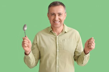 Yeşil arka planda gümüş kaşıklı olgun bir adam.