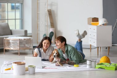 Beagle köpekli genç çift yeni evlerinde tamir sırasında dizüstü bilgisayar kullanıyor.