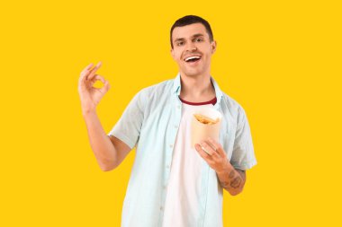 Patates kızartması tutan ve sarı arka planda iyi niyet gösteren genç bir adam.