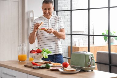 Orta yaşlı bir adam mutfakta çıtır tostlarla lezzetli sandviçler yapıyor.