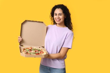 Sarı arka planda lezzetli pizzası olan güzel, mutlu, Afro-Amerikalı bir kadın.