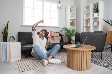 Mutlu, dövmeli, hediye çeki olan genç bir adam evde oturuyor.