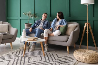 Oturma odasındaki gri koltukta oturan genç çift.