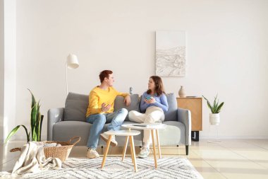 Genç çift evdeki gri kanepede sohbet ediyor.