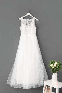 Gri duvarda güzel bir gelinlik ve beyaz tahta merdivende gelin buketi.