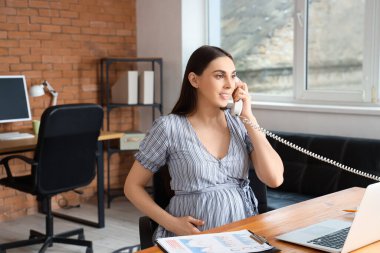 Hamile iş kadını ofiste telefonla konuşuyor.