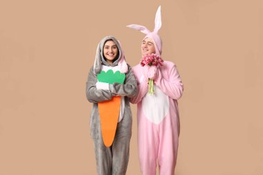 Kahverengi arka planda bir buket lale ve kağıt havuç olan tavşan kostümlü güzel bir çift. Paskalya kutlaması