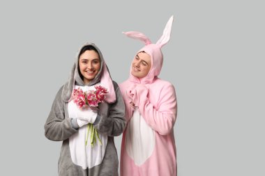Gri arka planda bir buket lale olan tavşan kostümlü güzel bir çift. Paskalya kutlaması