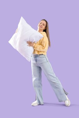 Young woman with soft pillow on lilac background