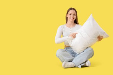 Sarı arka planda oturan yumuşak yastıklı genç kadın.