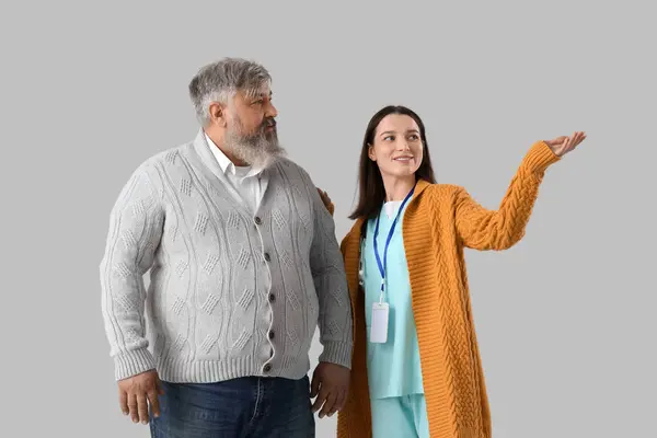 Mature man and nurse showing something on light background