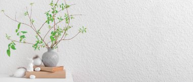 Ağaç dalları olan vazolar, Paskalya yumurtaları ve beyaz duvarın yanındaki masada tavşancık. Tasarım için pankart