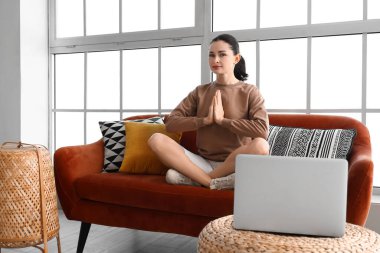 Evdeki kanepede meditasyon yapan güzel bir kadın.