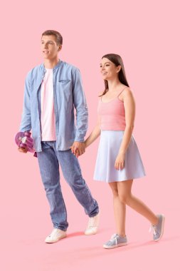 Pembe arka planda kaykayları olan mutlu genç çift.