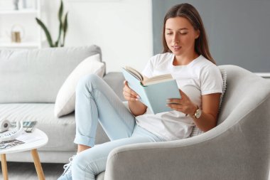 Evde boş gününde kitap okuyan genç bir kadın.