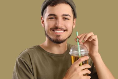 Yeşil arka planda bir bardak meyve suyu olan genç adam, yakın plan.