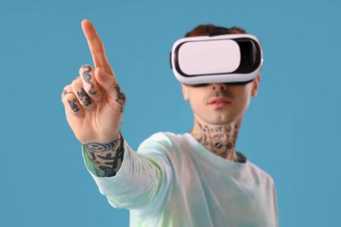 VR gözlüklü genç adam mavi arka planda sanal ekran kullanıyor, yakın plan.