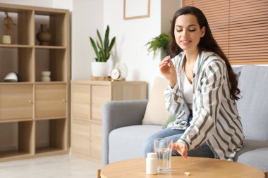 Bir bardak suyla evde ilaç alan genç bir kadın.