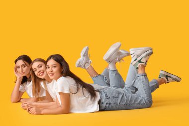 Sarı arka planda uzanan şık kotlu genç kadınlar.