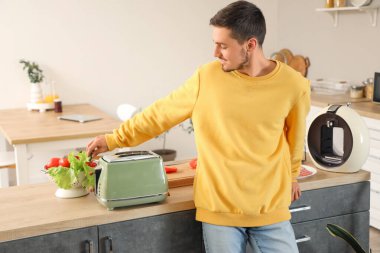 Modern tost makinesi ve taze sebzeli genç adam mutfakta.