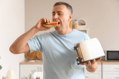 Tost makinesiyle orta yaşlı bir adam mutfakta lezzetli sandviçler yiyor.