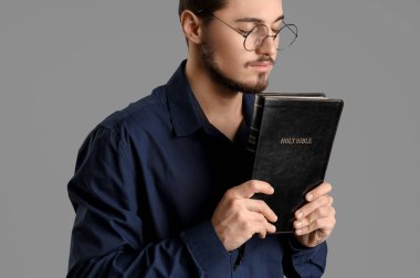 İncil 'i olan genç adam gri arka planda dua ediyor.