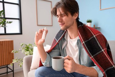 Hasta, genzinden damlayan ve evdeki kanepede oturan bir fincan çay içen genç adam.