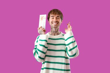 Hediye kartı olan dövmeli genç adam mor arka planda şans diliyor.