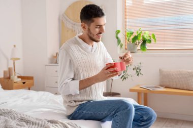 Yatak odasında kalp şeklinde çikolata şekerlemeleri olan yakışıklı bir adam.