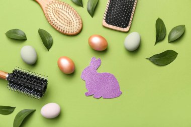 Yapraklı saç fırçaları, yeşil arka planda Paskalya yumurtaları ve kağıt tavşanlar.