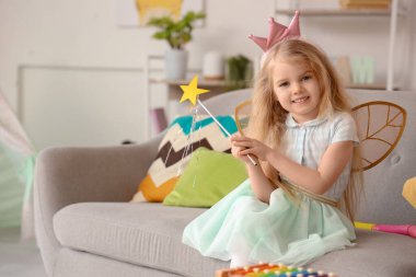 Evdeki kanepede oturan peri gibi giyinmiş şirin küçük kız.