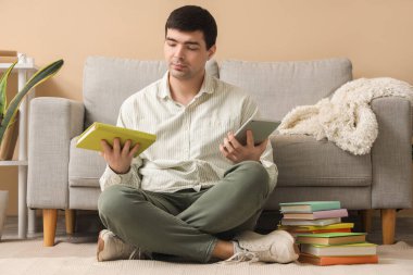 Kitaplı ve tabletli genç adam evde yerde oturuyor.