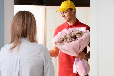 Erkek kurye kapıdaki kadına bir buket gül getiriyor.