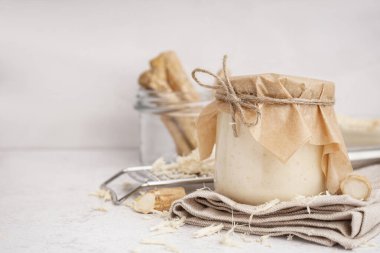 Beyaz arka planda yabanturpu kökleri olan yabanturpu sosu kavanozu.