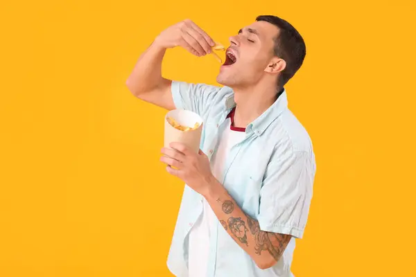 黄色の背景にフライドポテトを食べる若い男 — ストック写真