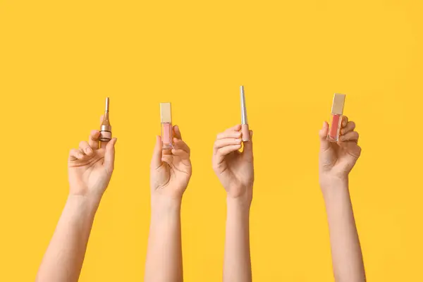 Female hands with lip glosses and eyeliners on yellow background