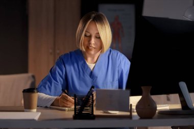 Not defteri olan kadın hemşire, akşam hastanede ders çalışıyor.