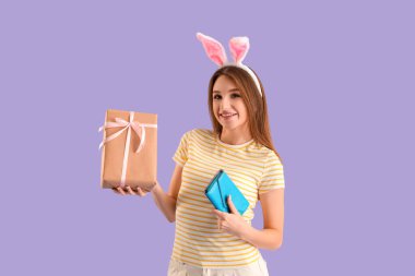 Leylak arka planında hediye kutusu ve cüzdanı olan tavşan kulaklı genç bir kadın. Paskalya Satışı