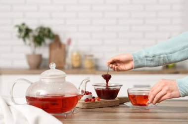 Genç bayan mutfakta kızılcık reçeli ile çay yapıyor.