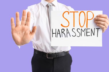 Elinde kağıt tutan bir işadamı. Leylak arkaplanında DUR HARASSMENT, yakın plan