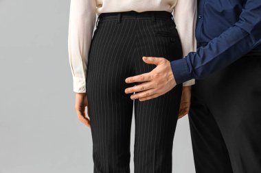 Business man touching his female colleague's butt on light background, closeup. Harassment concept