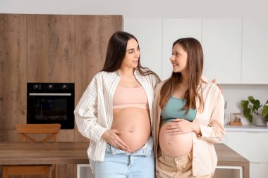 Hamile bayan arkadaşlar mutfakta sarılıyorlar.