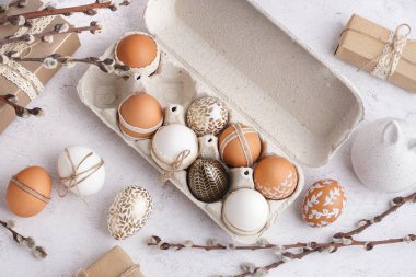 Süslü Paskalya yumurtaları, hediye kutuları ve beyaz arka planda söğüt dalları olan kağıt tutucu.