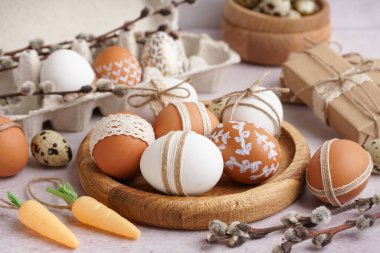 Süslü Paskalya yumurtaları, hediye kutuları, kağıt tutacağı ve beyaz arka planda söğüt dalları olan tahta tabaklar.