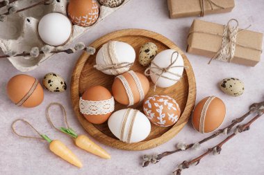 Süslü Paskalya yumurtaları, hediye kutuları, kağıt tutacağı ve beyaz arka planda söğüt dalları olan tahta tabaklar.
