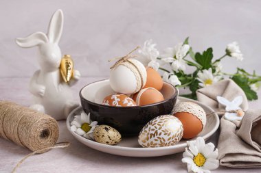Beyaz arka planda süslü Paskalya yumurtaları, tavşan ve bahar çiçekleri olan tabaklar.