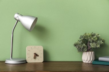 Bonsai ağacıyla ahşap masa, saat ve lamba yeşil arkaplan yakınlarında.