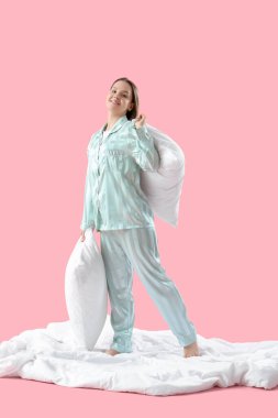 Pembe arka planda yumuşak yastıklı pijamalı genç bir kadın.