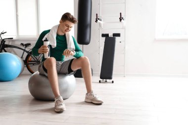 Spor salonunda elinde su şişesi olan genç bir adam fitball oynarken ukala bakışlarına bakıyor.