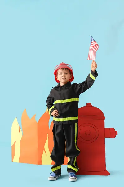 Cute little firefighter with USA flag and paper hydrant on blue background